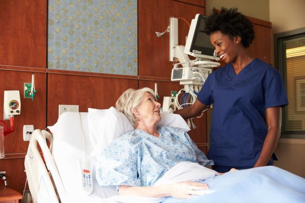 Nurse in dark blue scrubs comforting a senior female patient lying in a hospital bed