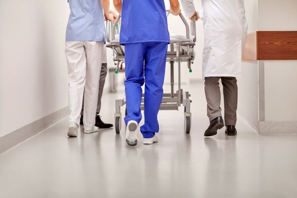Two nurses and a doctor wheeling a hospital bed through a hallway