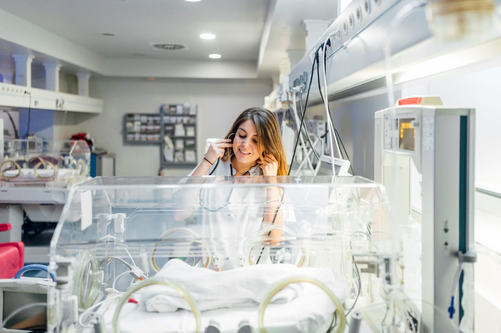 Family Nurse Practitioner puts on stethoscope in front of incubator with baby inside