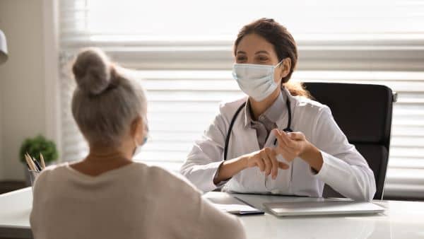 Nurse wearing a mask and chatting with elderly female patient