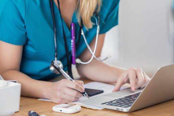 Close-up of a nurse in green scrubs writing notes down during a telehealth appointment