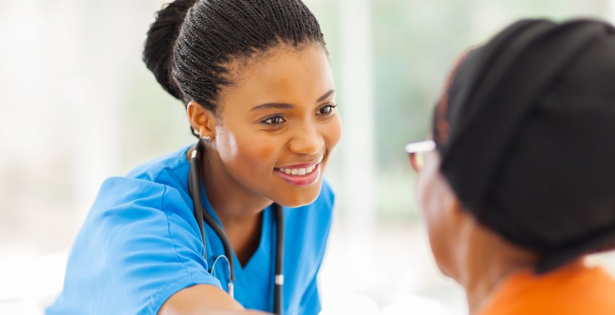 Smiling female African American nurse in blue scrubs comforting a female patient