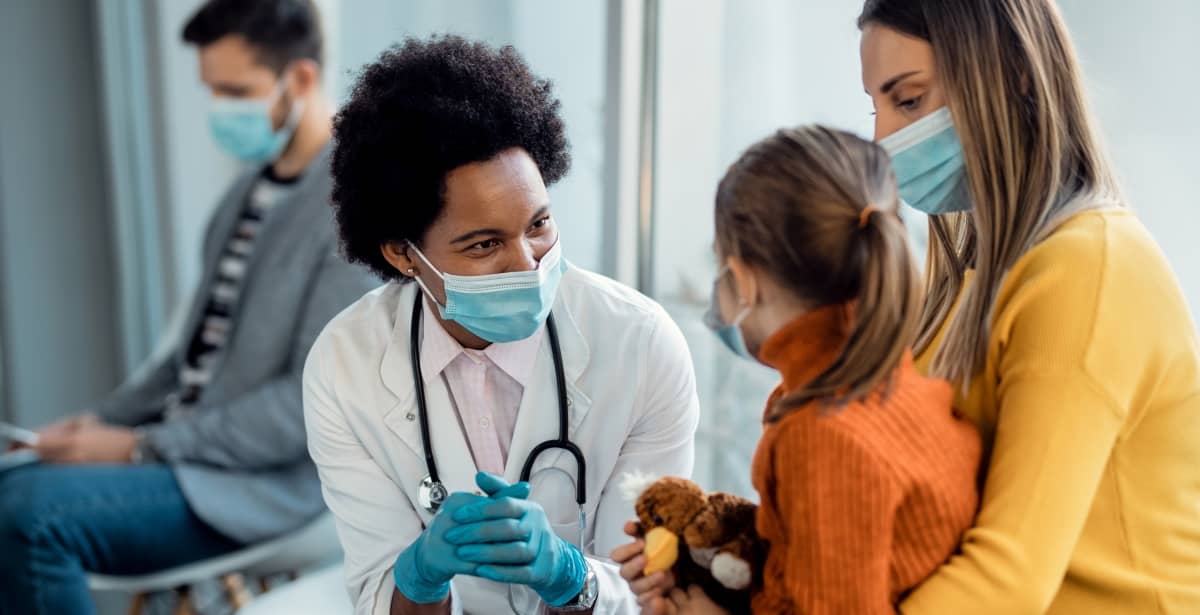 Nurse wearing a mask and chatting with young girl and mother