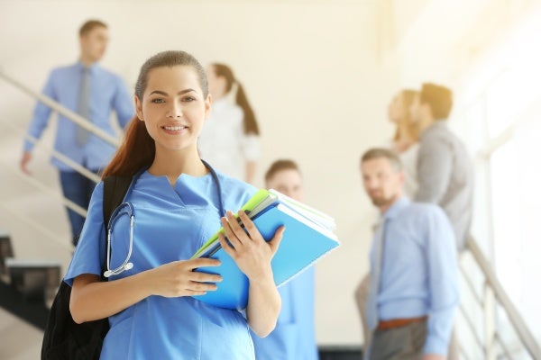 Female nurse wearing scrubs and holding notebooks while walking down the stairs with a group of well-dressed people behind her