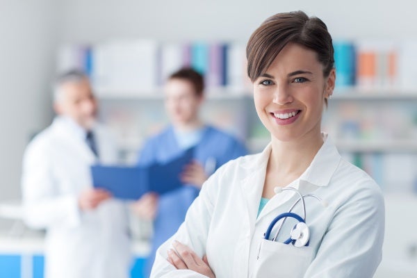 Smiling female nurse practitioner with a male nurse and doctor consulting charts in the background