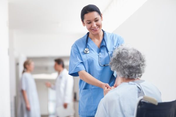 Female nurse in blue scrubs holding the hands of an elderly patient in a wheelchair