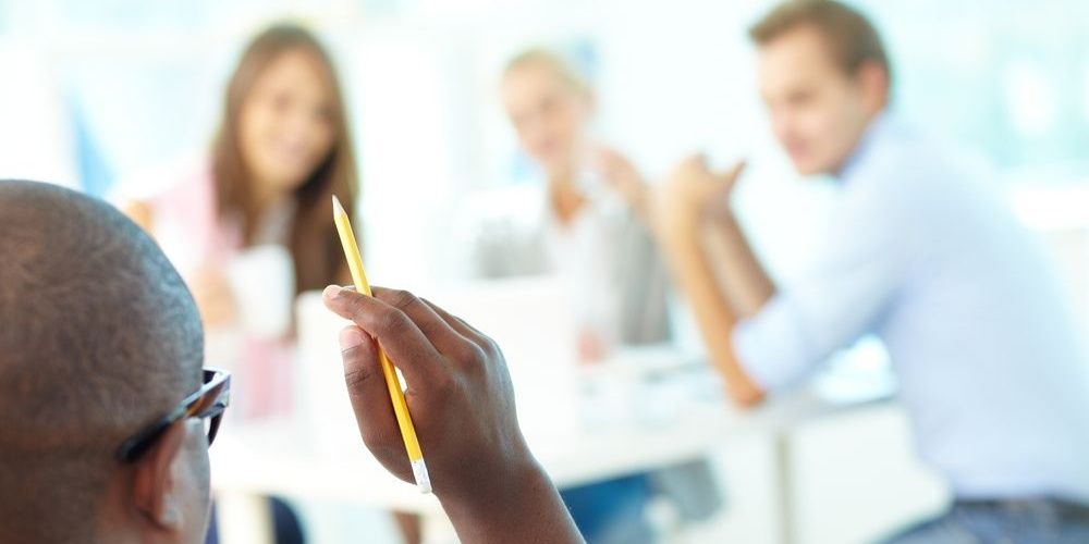 Back view of a man's head holding a pencil while chatting with other students in a cafeteria