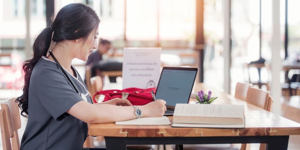 Nurse wearing scrubs and doing schoolwork in a library