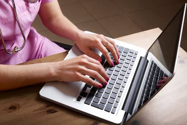 Nurse in pink scrubs researching nursing trends in 2024 on her laptop