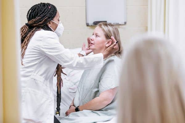 African American nurse wearing face mask and examining older Caucasian female