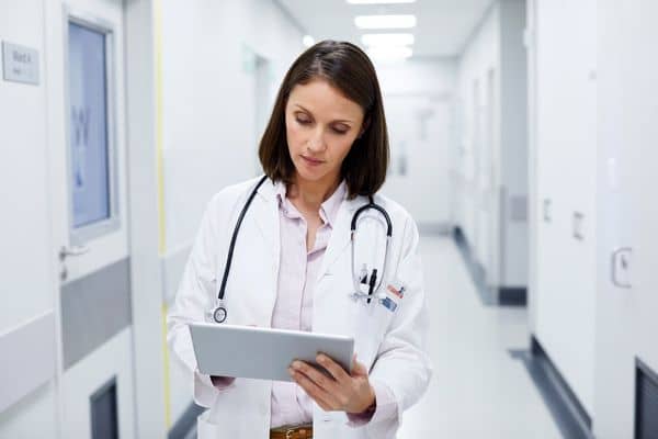 Confident female nurse practitioner reviewing patient notes in hospital hallway
