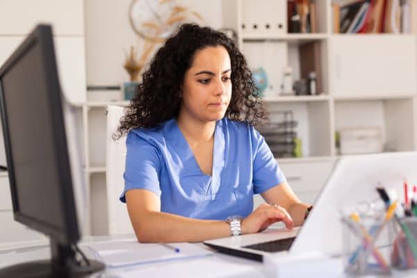 Nurse in blue scrubs looking up nursing trends in her office