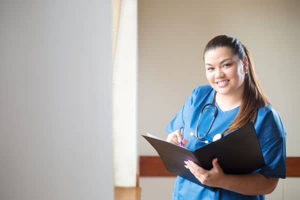 Smiling nurse in blue scrubs, making notes