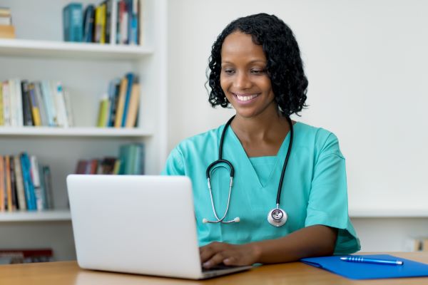 Smiling African American nurse in green scrubs typing on a computer in her home office