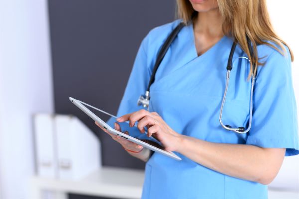 Close-up of a nurse in blue scrubs using a tablet device