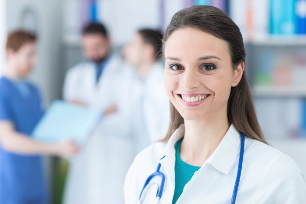 Smiling nurse practitioner in a white lab coat with a blue stethoscope around her neck