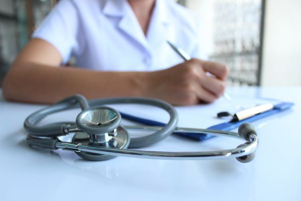 Close-up of a nurse practitioner writing on a clipboard with a stethoscope in front of her