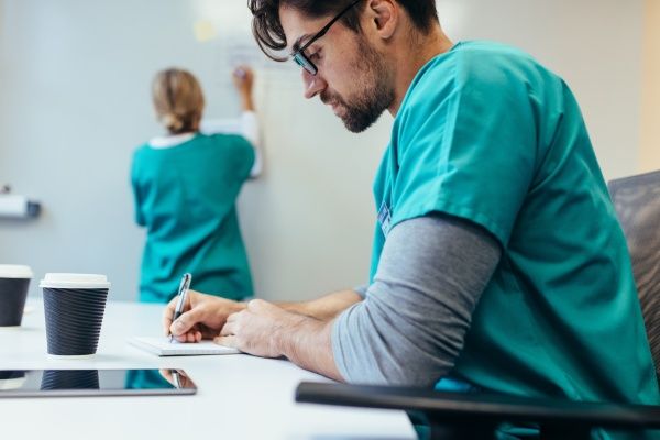 Male nurse making notes at a desk with his female colleague behind him