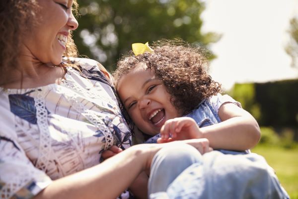 Smiling mother holding her laughing daughter in a bright outdoor park