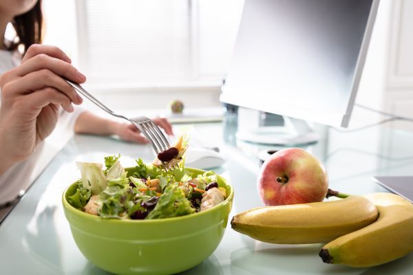 Close-up of a woman eating a salad and fruit in a brightly lit office