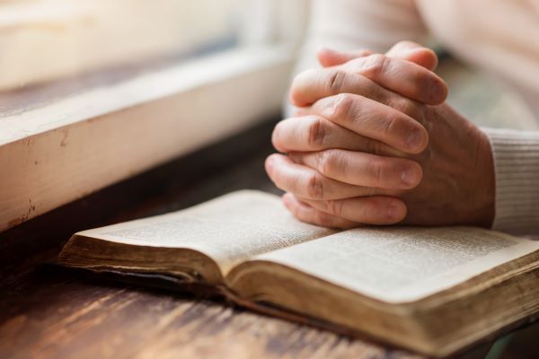 Close-up of a pair of hands clasped on top of a book on a wooden desk