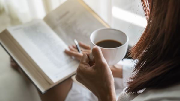 A woman reading a book while sipping a coffee