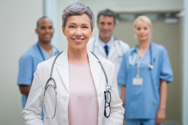 Older female nurse practitioner smiling and looking confident in front of a group of health care workers