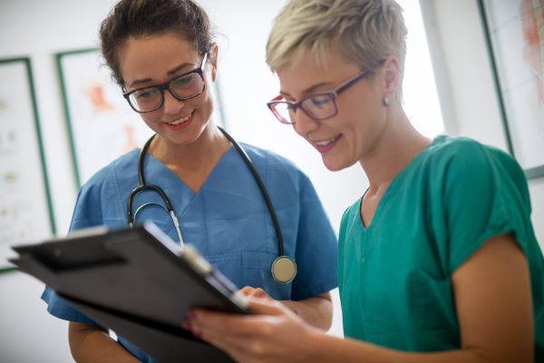 Two nurses looking over a patient's health records on a clipboard