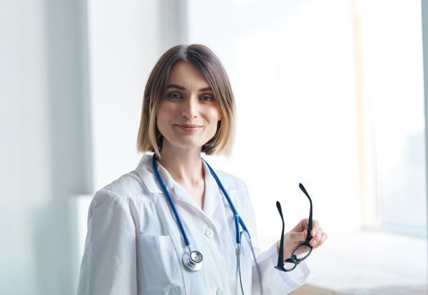 Smiling nurse practitioner in her brightly lit office holding a pair of glasses